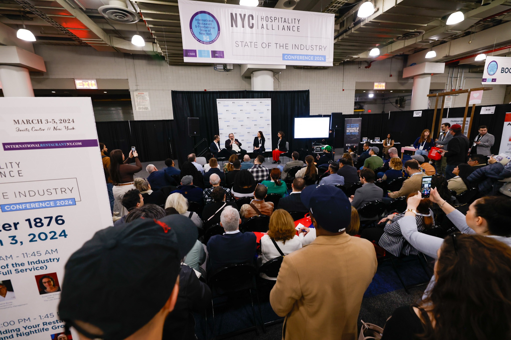 A large group of people seated and standing at a conference attending a presentation.